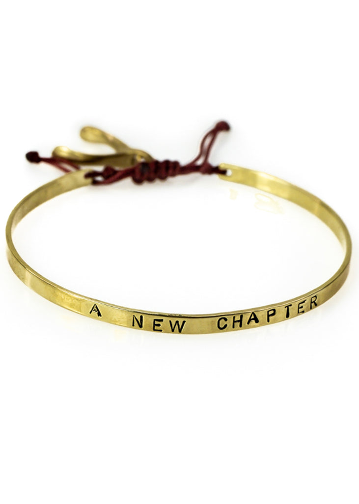 Handmade, gold, adjustable bracelet, which ties with a black cord, stamped with the phrase A New Chapter