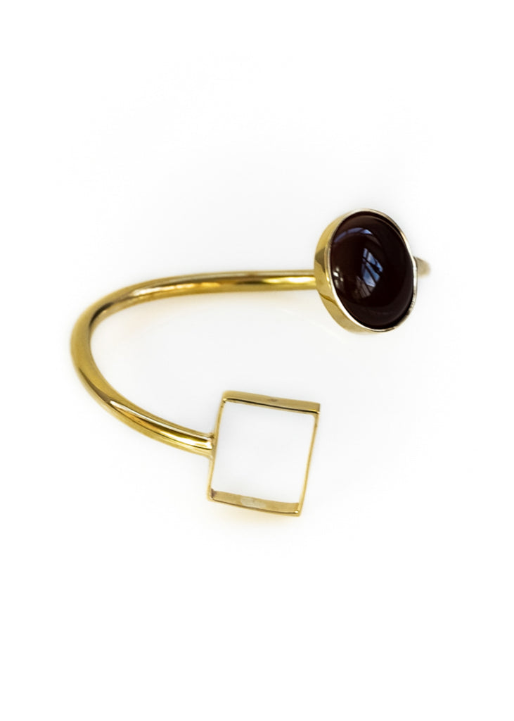 Photo of a gold, spiral shaped bracelet, with a black stone on one end and a square on the other