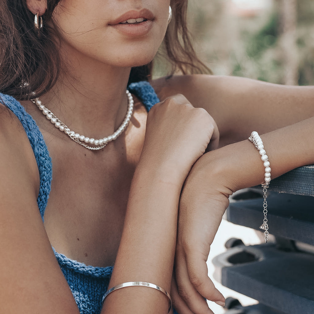 Female in a blue knitted top. She is wearing a silver chain and pearls necklace, and bracelet