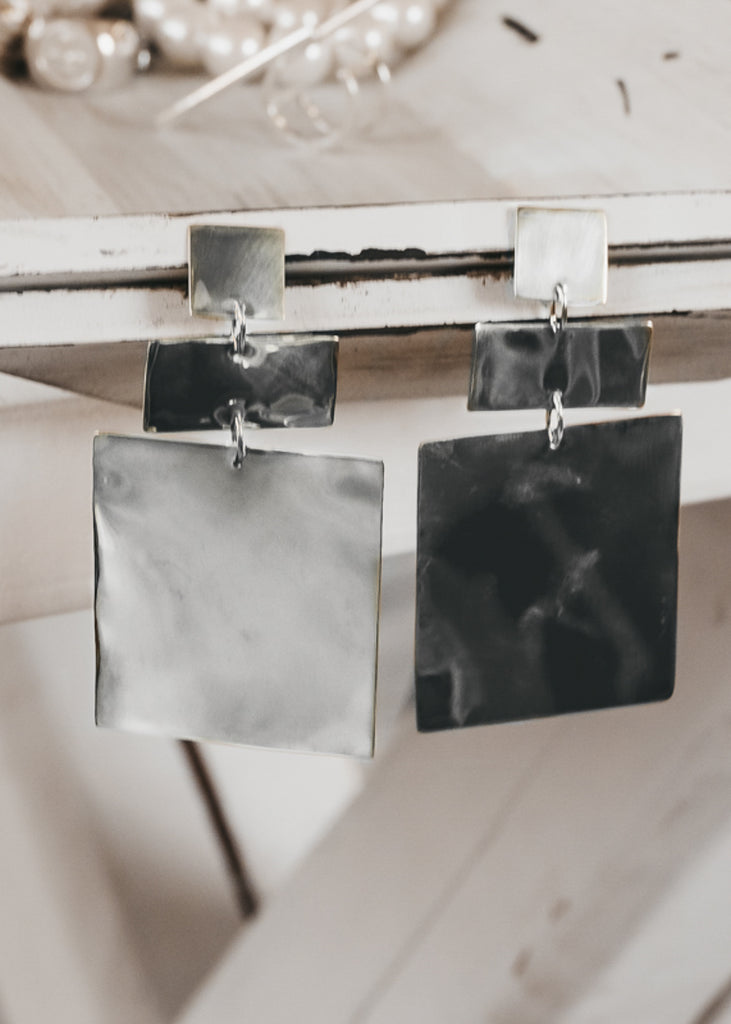 Silver, geometric shaped, pendant earrings pinned in between two white wooden plates