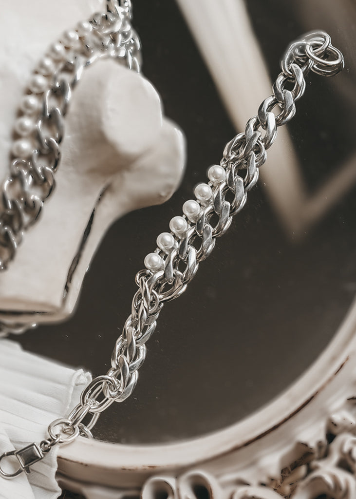 Marylin. Silver chain, and pearls bracelet, placed on a mirror.