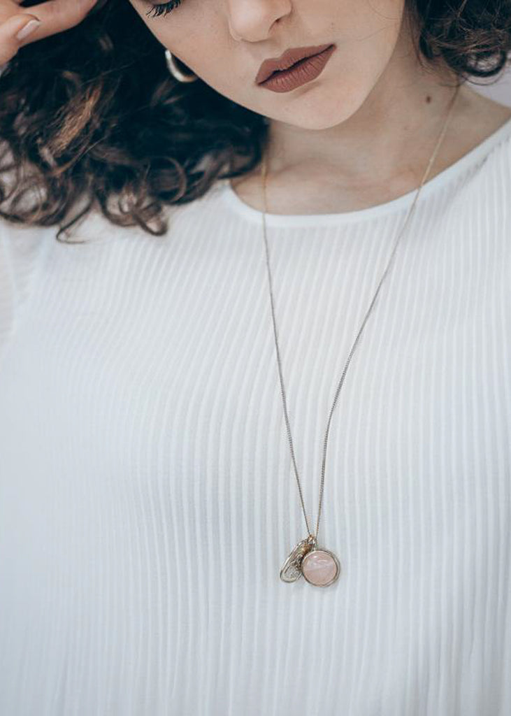 Brunette girl in a white blouse. She is wearing a long, silver chain necklace with a silver plaque and a pink quartz stone