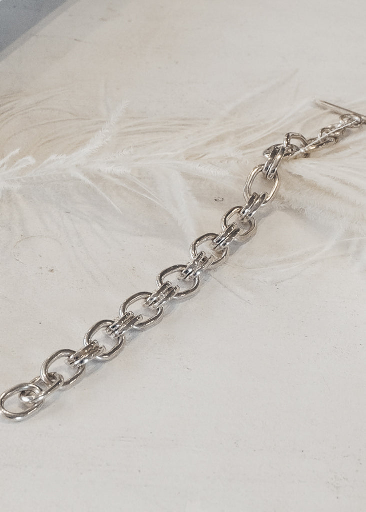 Silver, double link bracelet, placed on a white feathered surface