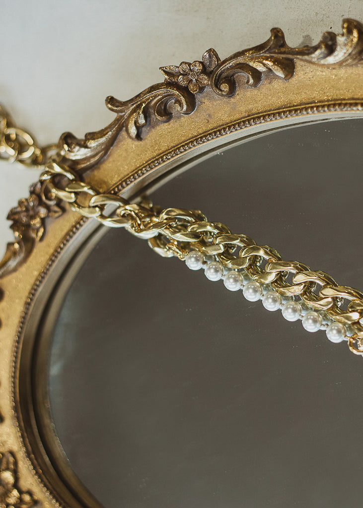 Gold, curb link chain and pearls necklace, placed on a vintage mirror