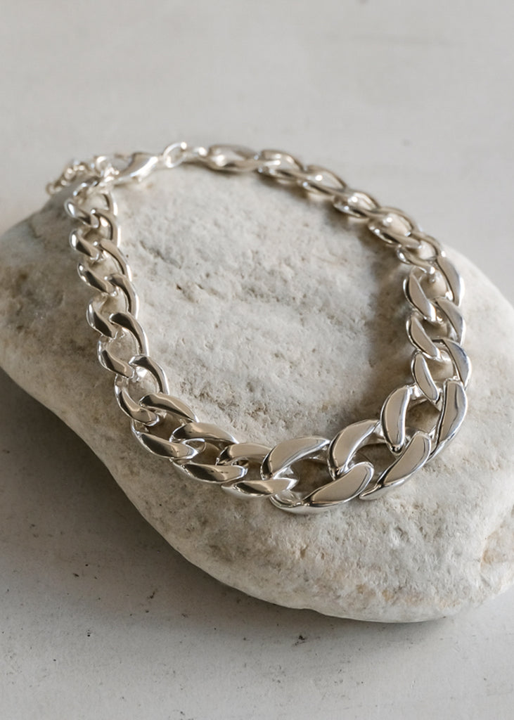 Mangata Small. Silver, chunky chain necklace placed on a white rock