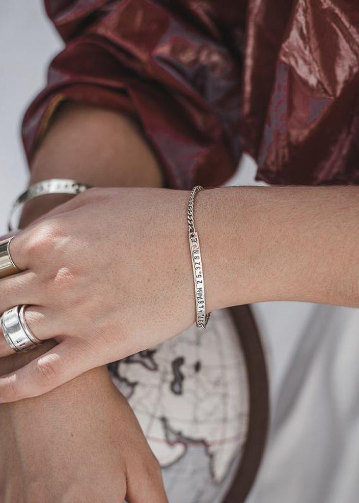 woman with white dress wearing  3rd Floor Arrival ID bracelet silver bracelet stamped with your choice of longitude and latitude coordinates
