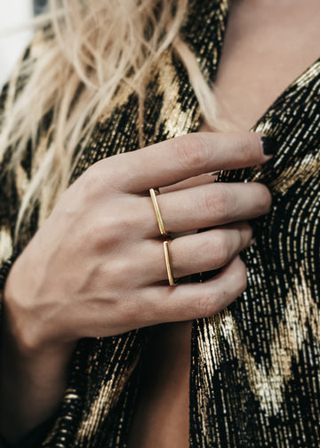 Close up of female's hand, wearing two, gold, straight line rings on her middle, and wedding ring fingers 