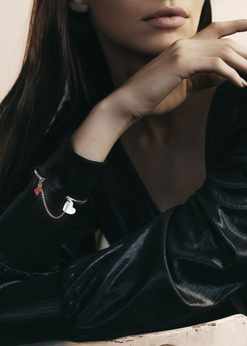 Close up of a female's right forearm. She is wearing a black, cuff blouse. Over the blouse's sleeve, she is wearing a silver, bangle and chain charm bracelet