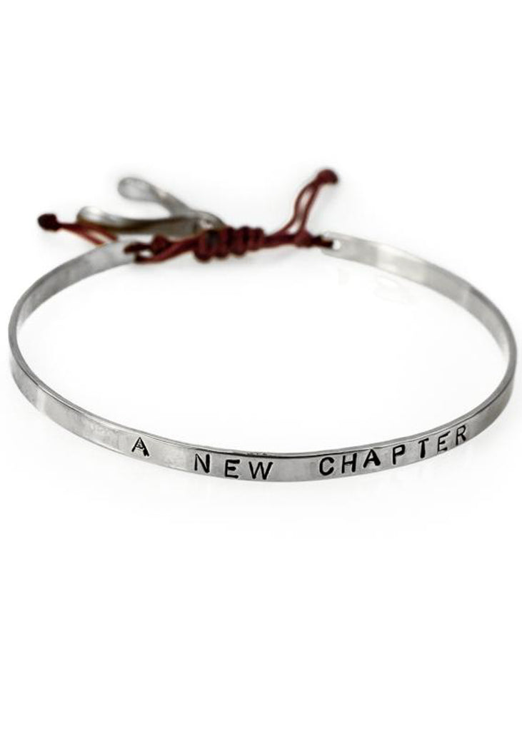 Handmade, silver, adjustable bracelet, which ties with a red cord, stamped with the phrase A New Chapter