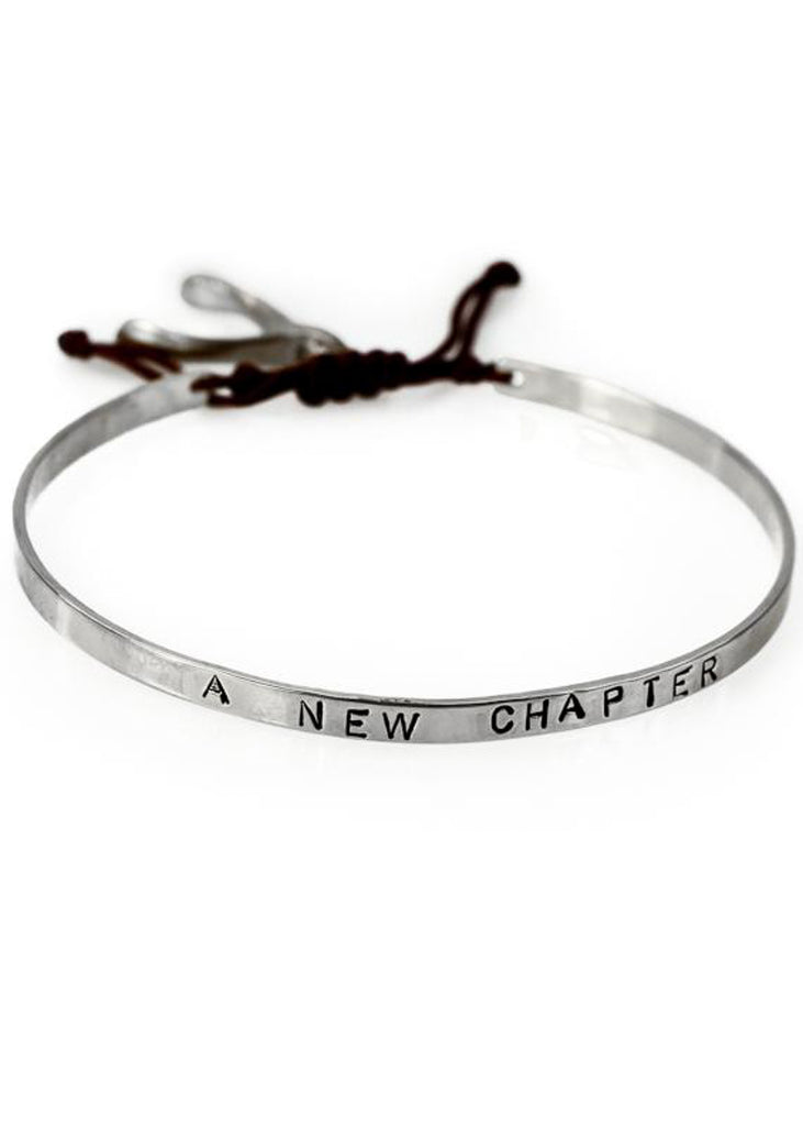 Handmade, silver, adjustable bracelet, which ties with a black cord, stamped with the phrase A New Chapter