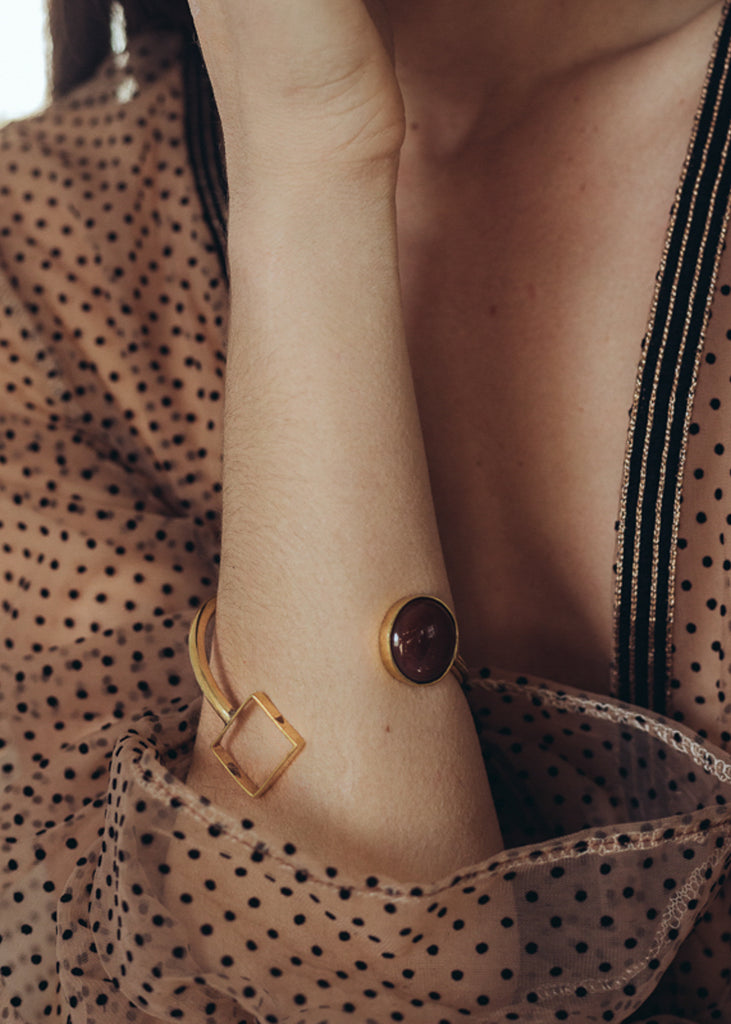 Χέρι μοντέλου που φοράει το χρυσό βραχιόλι Felicity με καφέ καρνεόλη.