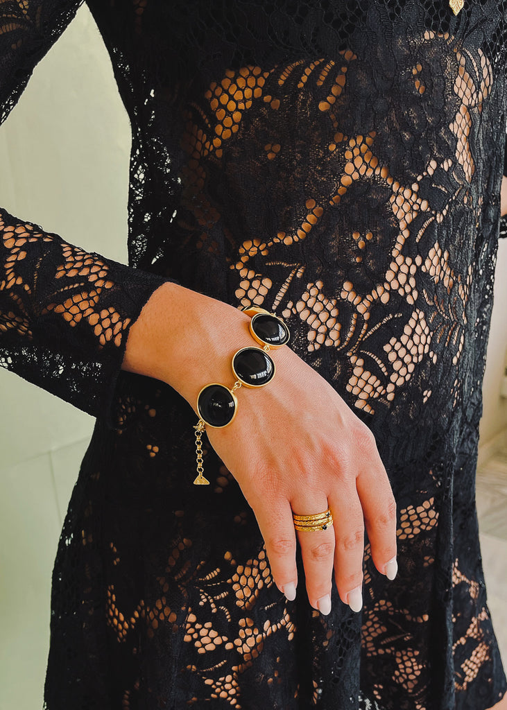 Female in black outfit. On her right hand, she is wearing a gold bracelet, with round, black stones