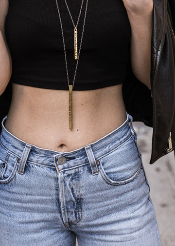 close-up woman's belly with Gold plated destination square rod chain necklace stamped with earth's coordinates 