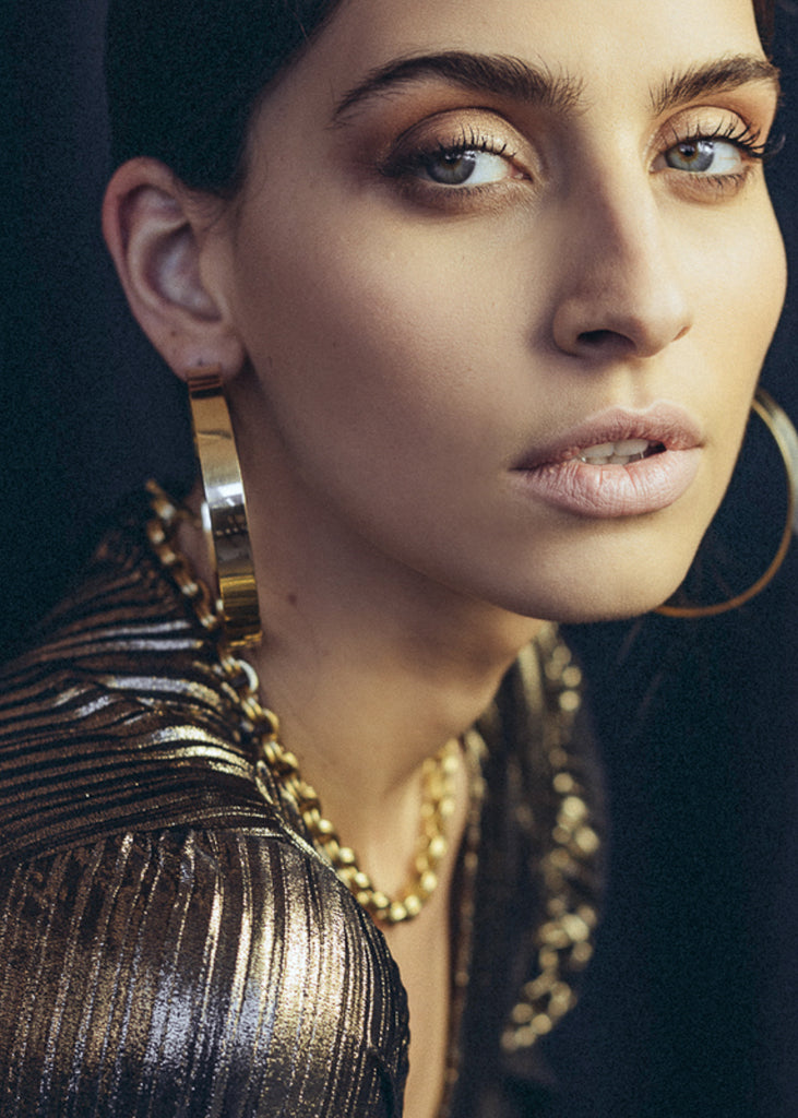 Beautiful female looking into the camera. She is wearing a pair of gold, wide, loop earrings