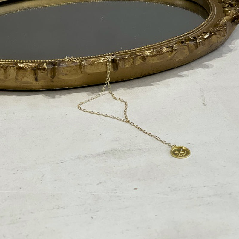 Gold plated sterling silver tie necklace, on a white table next to a gold mirror