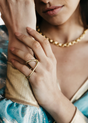 Female in sky blue and gold blouse. On her left hand fingers, she is wearing a gold, Alvaro, statemetn ring