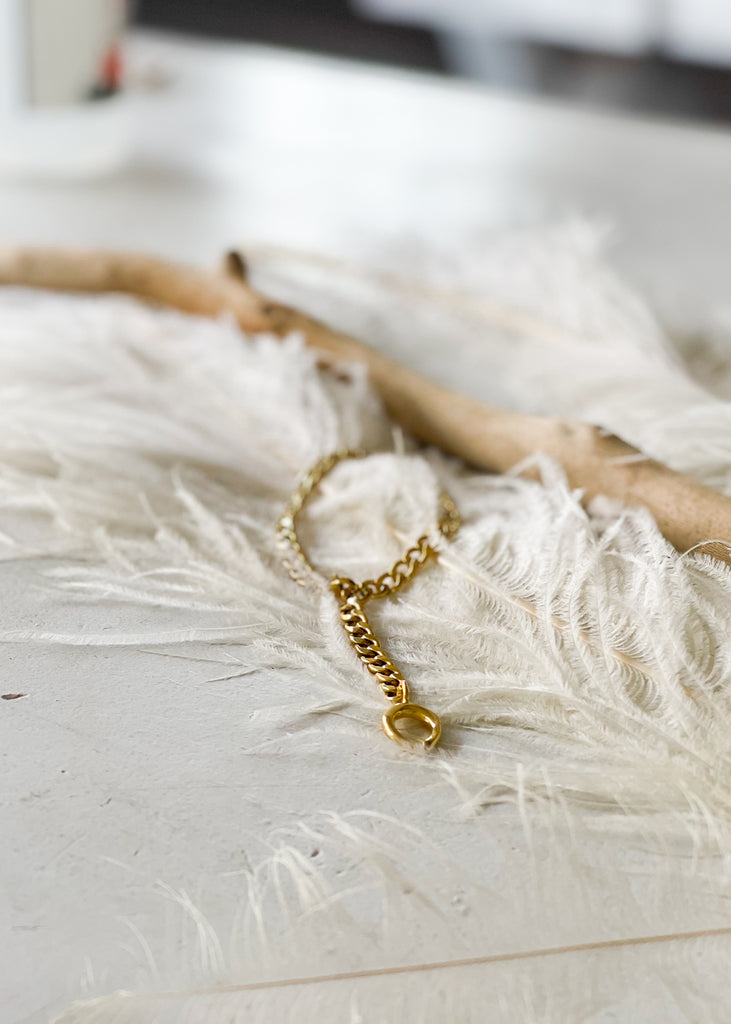 Gold, curb link anklet, with a dangling horseshoe charm, laying on a white feather.Χειροποίητο Βραχιόλι Ποδιού Fortunata Χρυσό