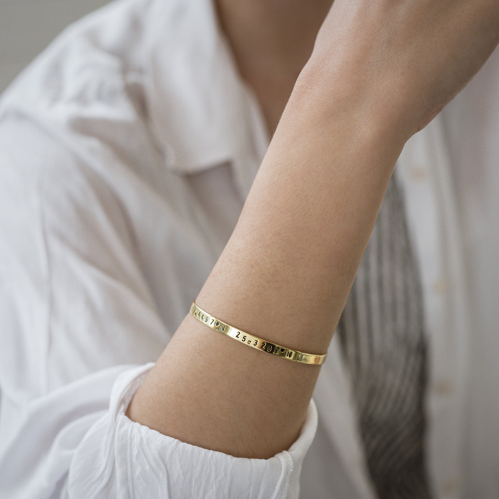 close-up female's arm, with, Gold plated adjustable bracelet stamped with earth's longitude and latitude coordinates
