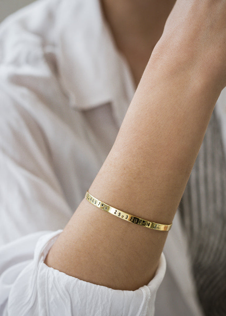 close-up female's arm, with, Gold plated adjustable bracelet stamped with earth's longitude and latitude coordinates