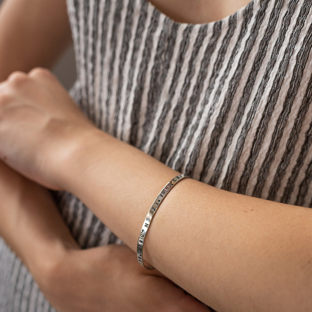 close-up female's arm, with, platinum-plated,adjustable bracelet stamped with earth's longitude and latitude coordinates