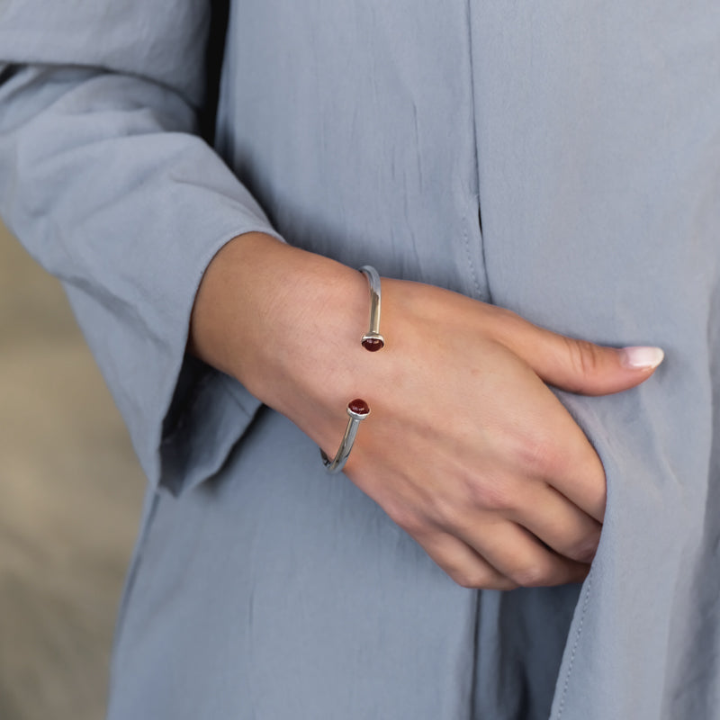 Female with her right hand fingers sliding into the pocket of her dress. On her wrist, a silver, adjustable bracelet with brown carnelian stones