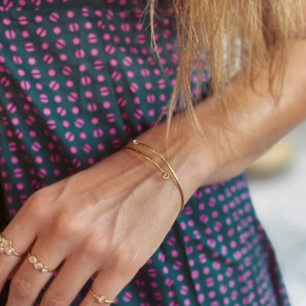 Χέρι γυναικείο που φοράει Χειροποίητο βραχιόλι Eday χρυσό με πέτρες Swarovski στις άκρες ροζ, και τρία δαχτυλίδια με ροζ πέτρες. 