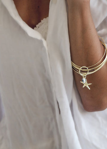 Female arm, bend over chest, with a gold bangle bracelet, with a starfish charm