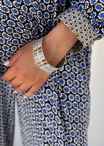 Female's arm, in a blue dress, leaned over the back of a chair. She is wearing a silver, statement cuff bracelet