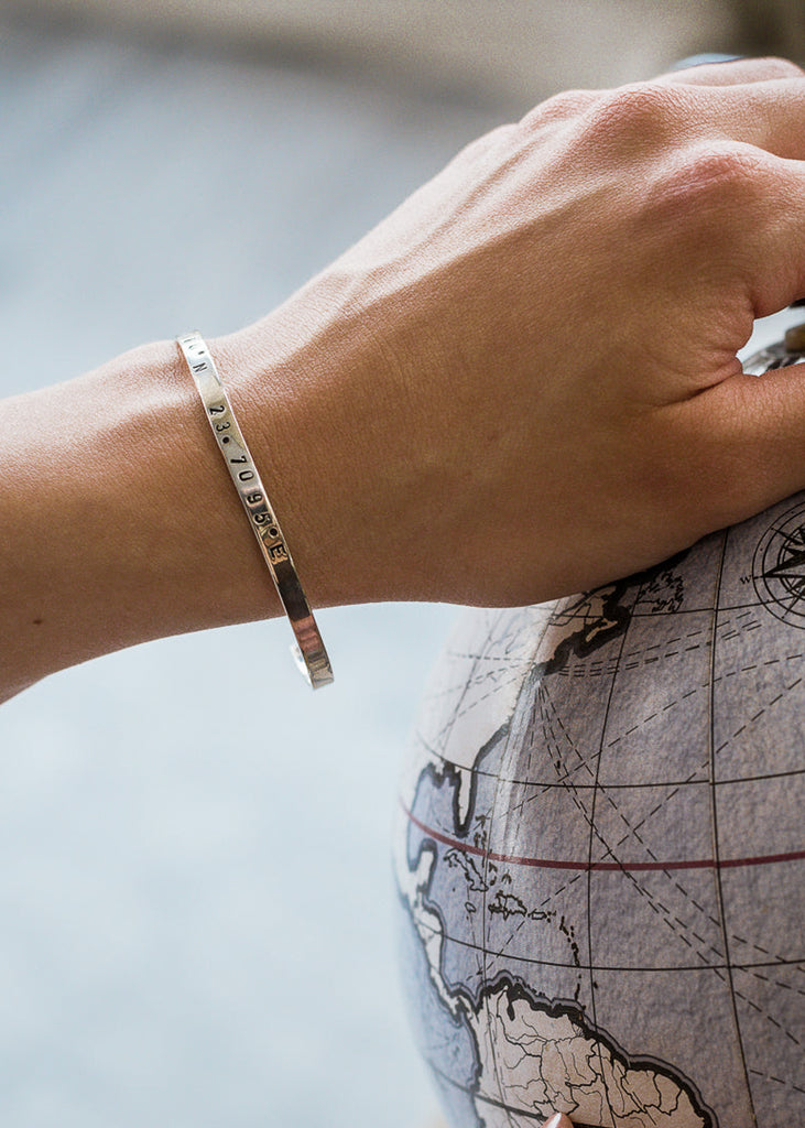 Female's hand, touching a decorative globe. She is wearing a silver, coordinates bracelet