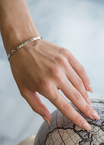 Female hand, in nude manicure, gently touching a decorative globe. She is wearing a silver, bangle bracelet