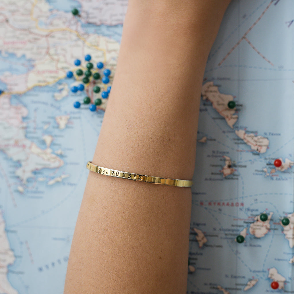 close-up model's arm, with, Gold plated adjustable bracelet stamped with earth's longitude and latitude coordinates
