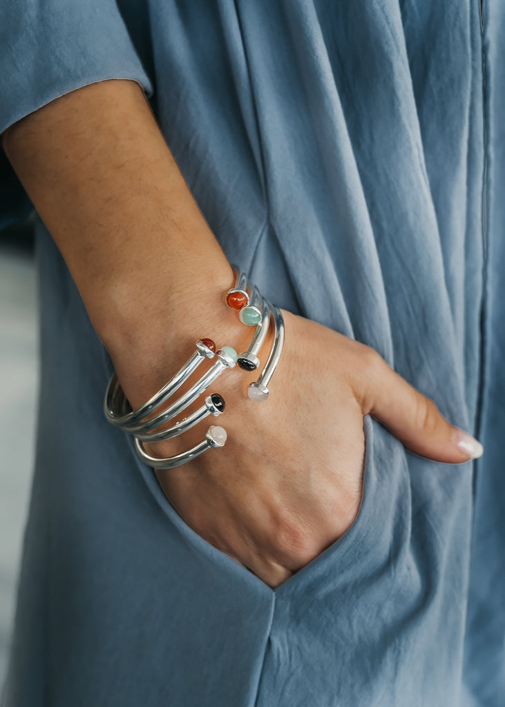 Female's hand in the pocket of her dress. On her wrist three silver bracelets, with semi precious stones are worn