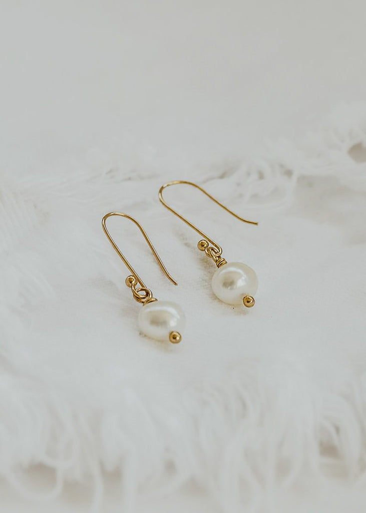 Two gold earrings with one small pearl hangind on each placed on a white background.