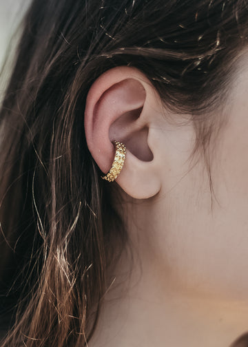 Brunette female's right profile. Close up of her ear, on which she is wearing a gold, embossed, ear cuff by 3rd Floor