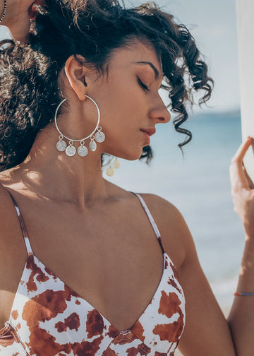 model is wearing a silver, loop earrings, with small, dangling coins