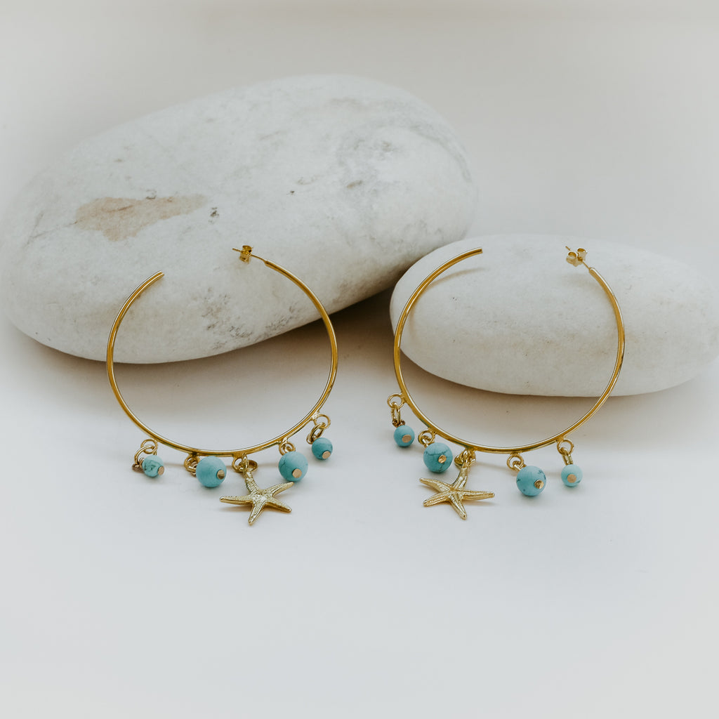 Two gold earrings consisting of a large thin hoop , a gold starfish charm and four round turqoise beads each. 