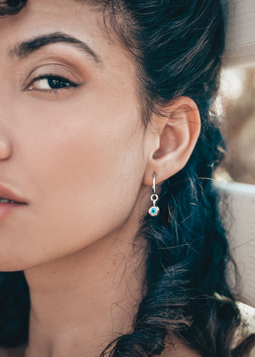model with a Pair of silver loop earring, with a hanging evil eye
