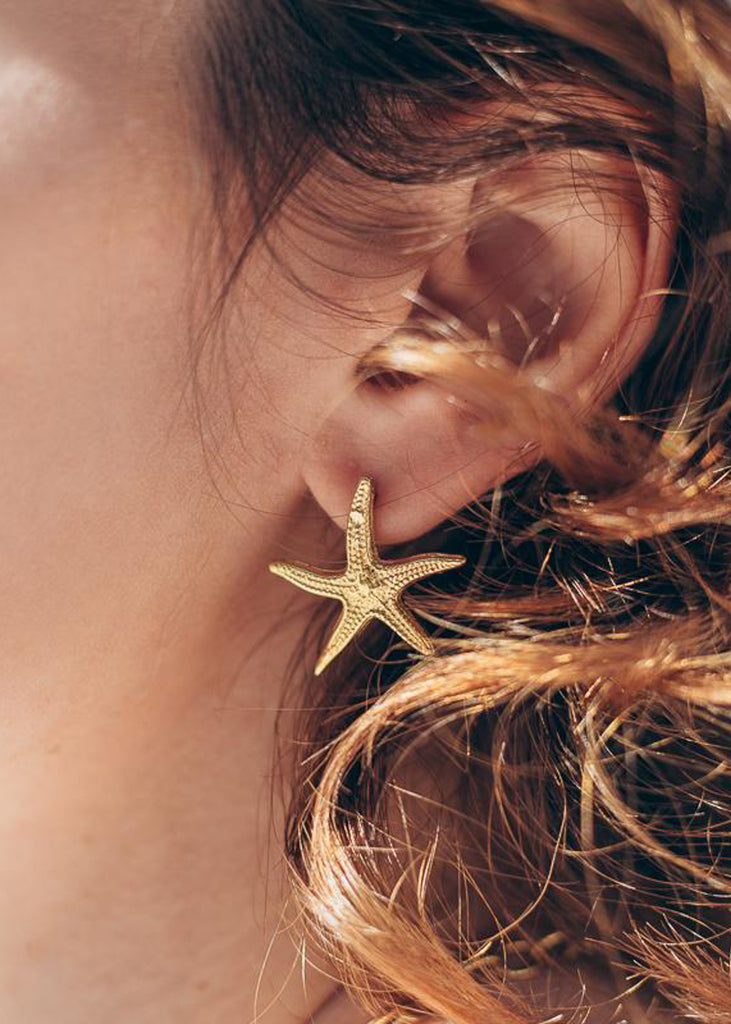 girl in profile. On her right ear, she is wearing a gold plated silver, starfish earring