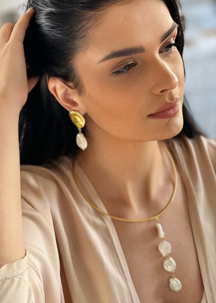 woman with beige top is wearing the Theros earrings in gold color and the Theros handmade necklace