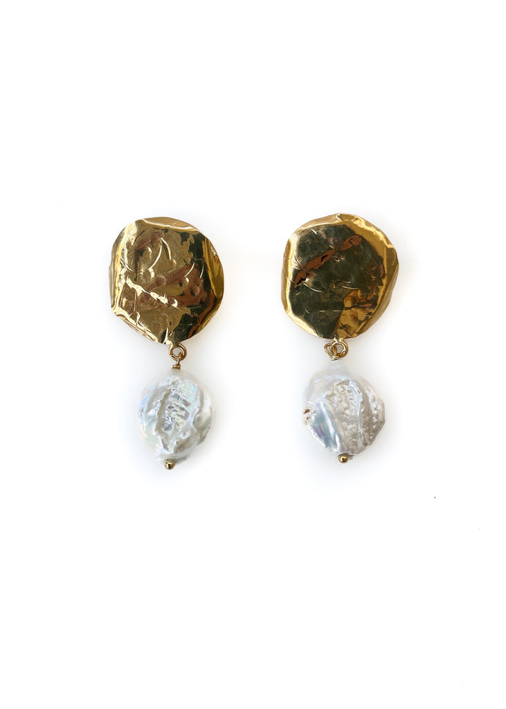 pair of the Theros drop earrings with a textured disk in gold color and an iridescent pearl hanging