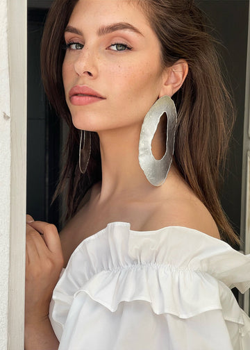 woman with a white top is wearing on her ears the Toma earrings in silver