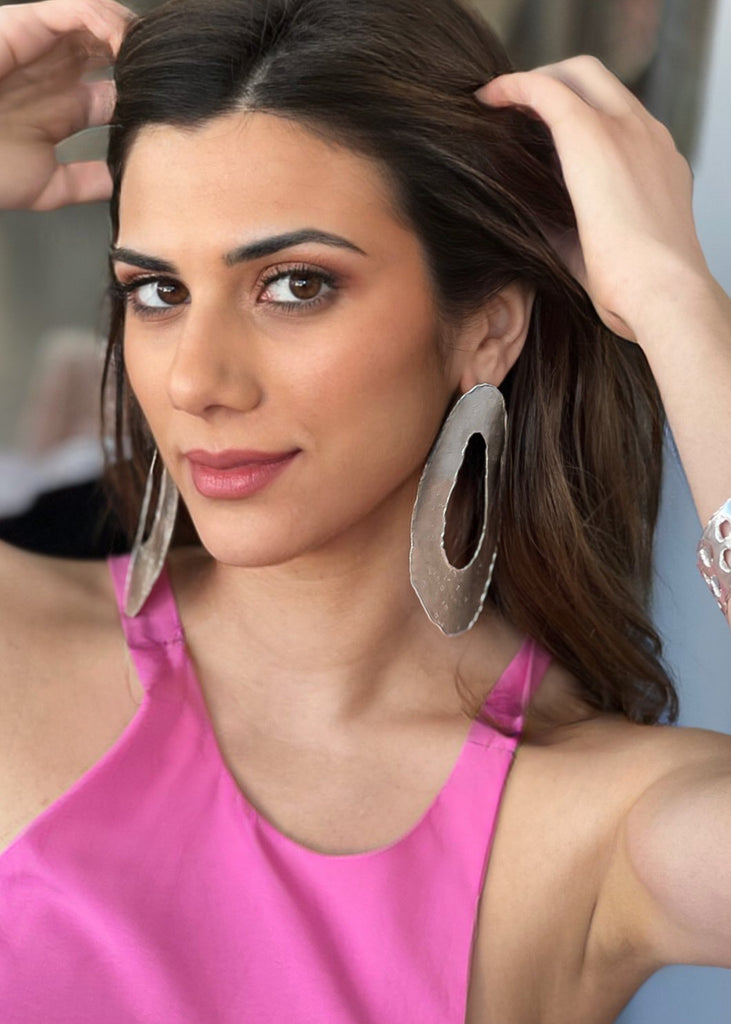 woman with a hot pink dress is holding her hair up showing her Toma statement earrings in silver color