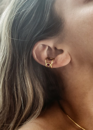 Αυτί γυναικείου μοντέλου που φοράει χειροποίητο ear cuff σκουλαρίκι χρυσό με μία πέτρα Swarovski κόκκινη.