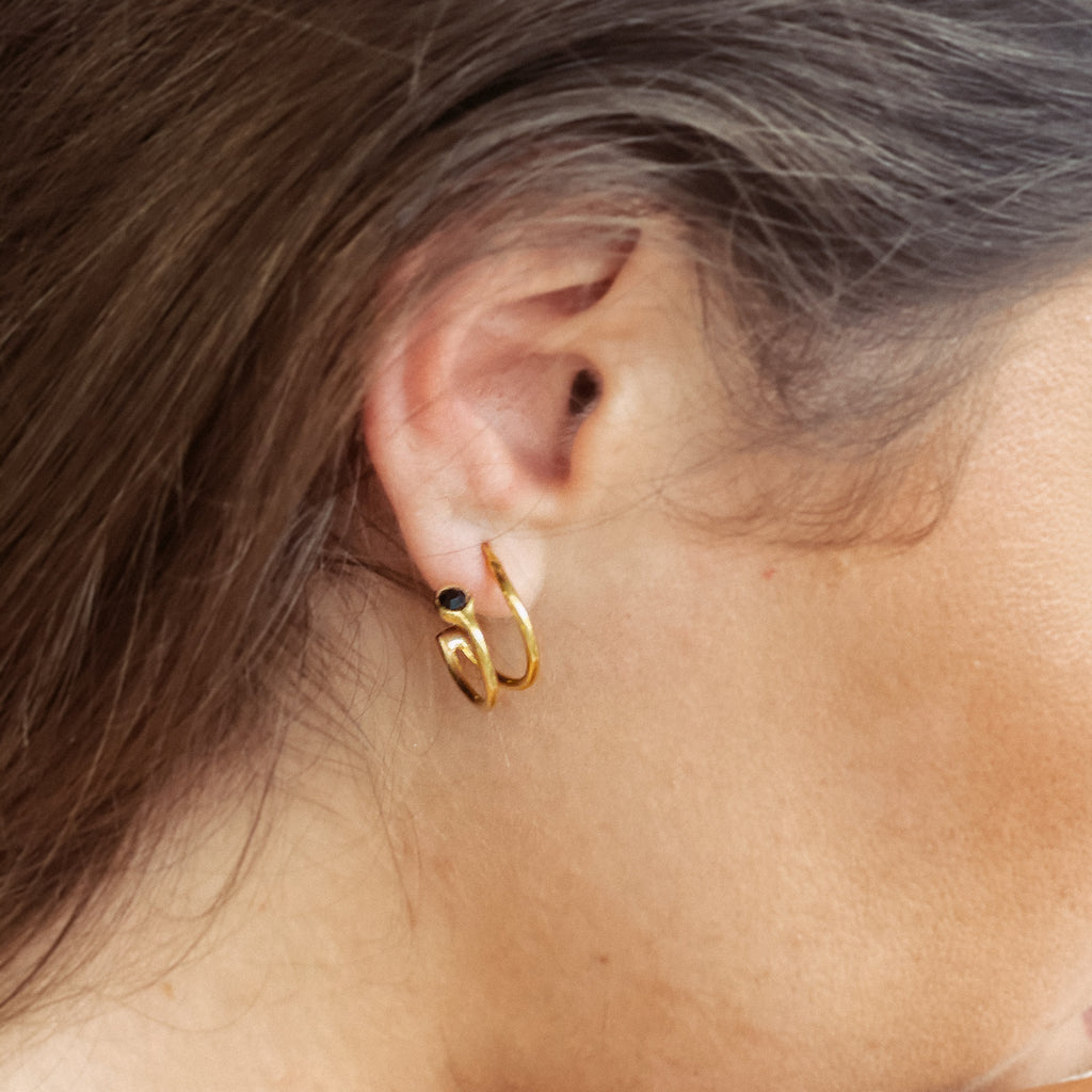 Χειροποίητο σκουλαρίκι Eday χρυσό με μία πέτρα Swarovski μαύρη, φορεμένο στο αυτί μοντέλου.