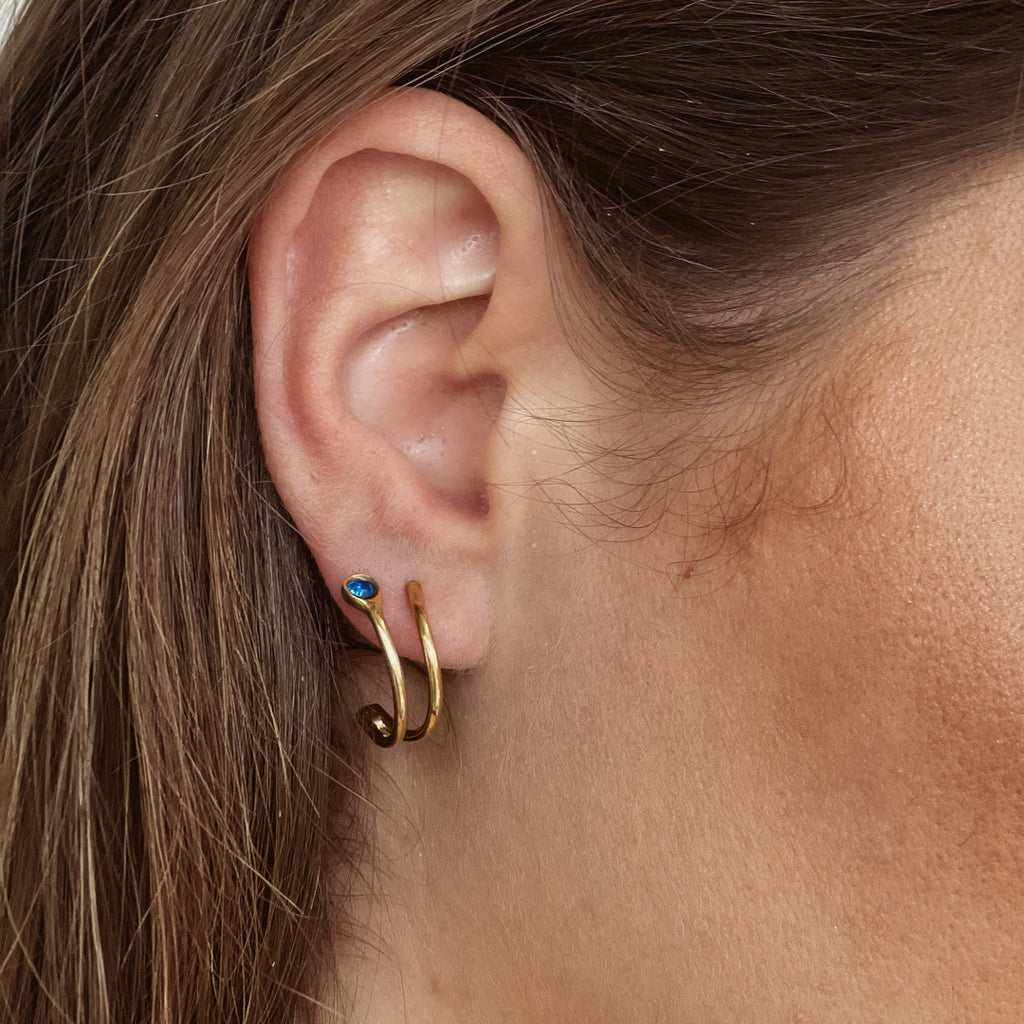 Χειροποίητο σκουλαρίκι Eday χρυσό με μία πέτρα Swarovski μπλε, φορεμένο στο αυτί μοντέλου.