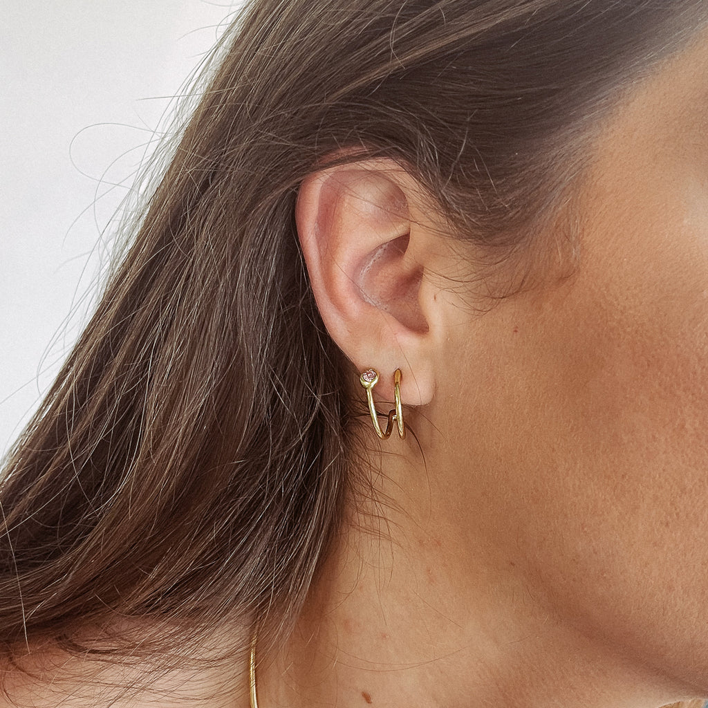 Χειροποίητο σκουλαρίκι Eday χρυσό με μία πέτρα Swarovski ροζ, φορεμένο στο αυτί μοντέλου.