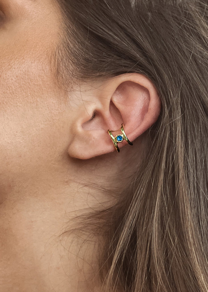 Μοντέλο που φοράει χειροποίητο ear cuff σκουλαρίκι χρυσό με μία πέτρα swarovski μπλε, στο αυτί.