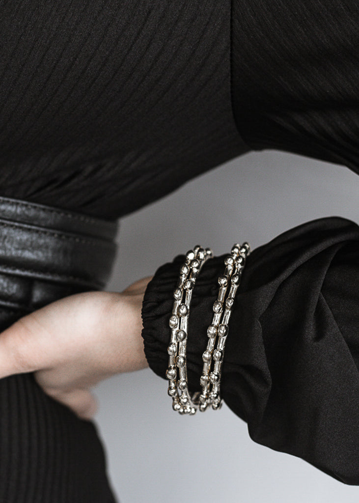 Close up of woman's left hand, resting backwards on her hip. She is wearing four silver bracelets