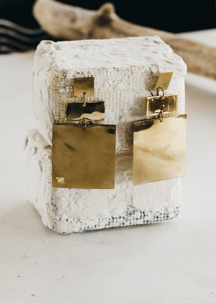Gold, geometric shaped, pendant earrings pinned on a white chalk brick