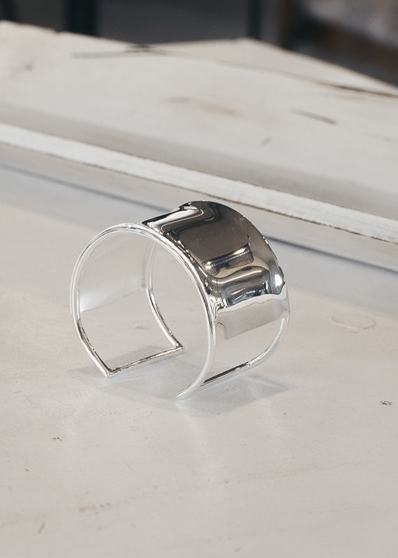 Fallon. Wide, silver, adjustable, statement cuff, on a white wooden surface